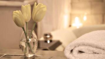 Un baño con un jarrón de tulipanes blancos sobre un mueble, una toalla blanca y una bañera.