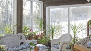 A sunroom with wicker furniture, large windows, and potted plants. - Inn at Ellis River (Jackson)