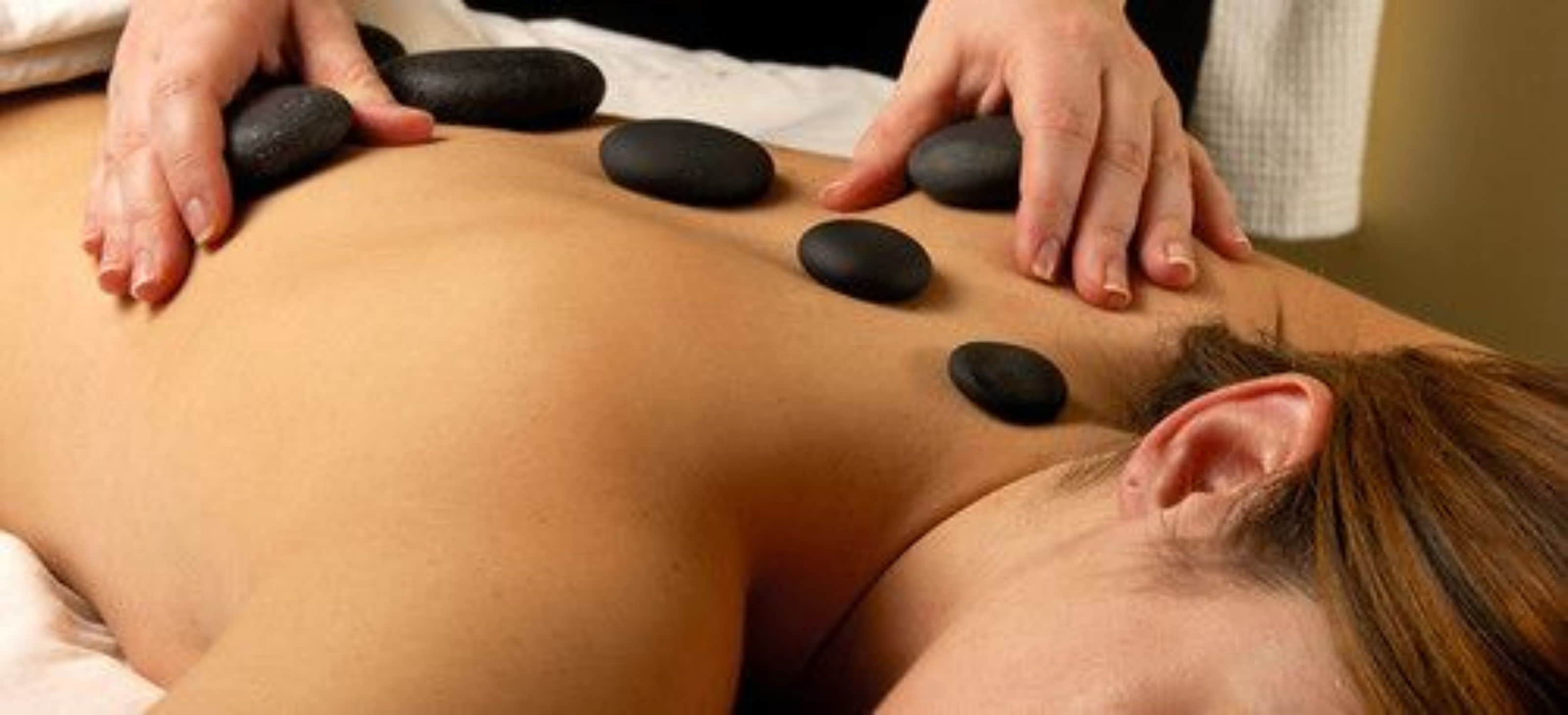 A massage therapy session with a person lying face down receiving pressure from stones on their back.
