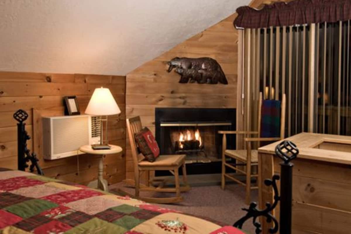 A cozy room with a fireplace, wooden walls, a quilted bedspread, and a lamp.