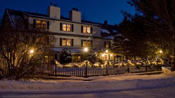 A two-story house with a snow-covered front yard and a fence. - Inn at Ellis River (Jackson)