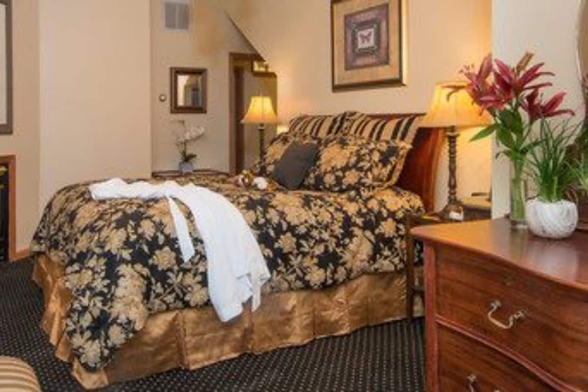 A hotel room with a bed, a fireplace, a nightstand, a dresser, and a mirror.