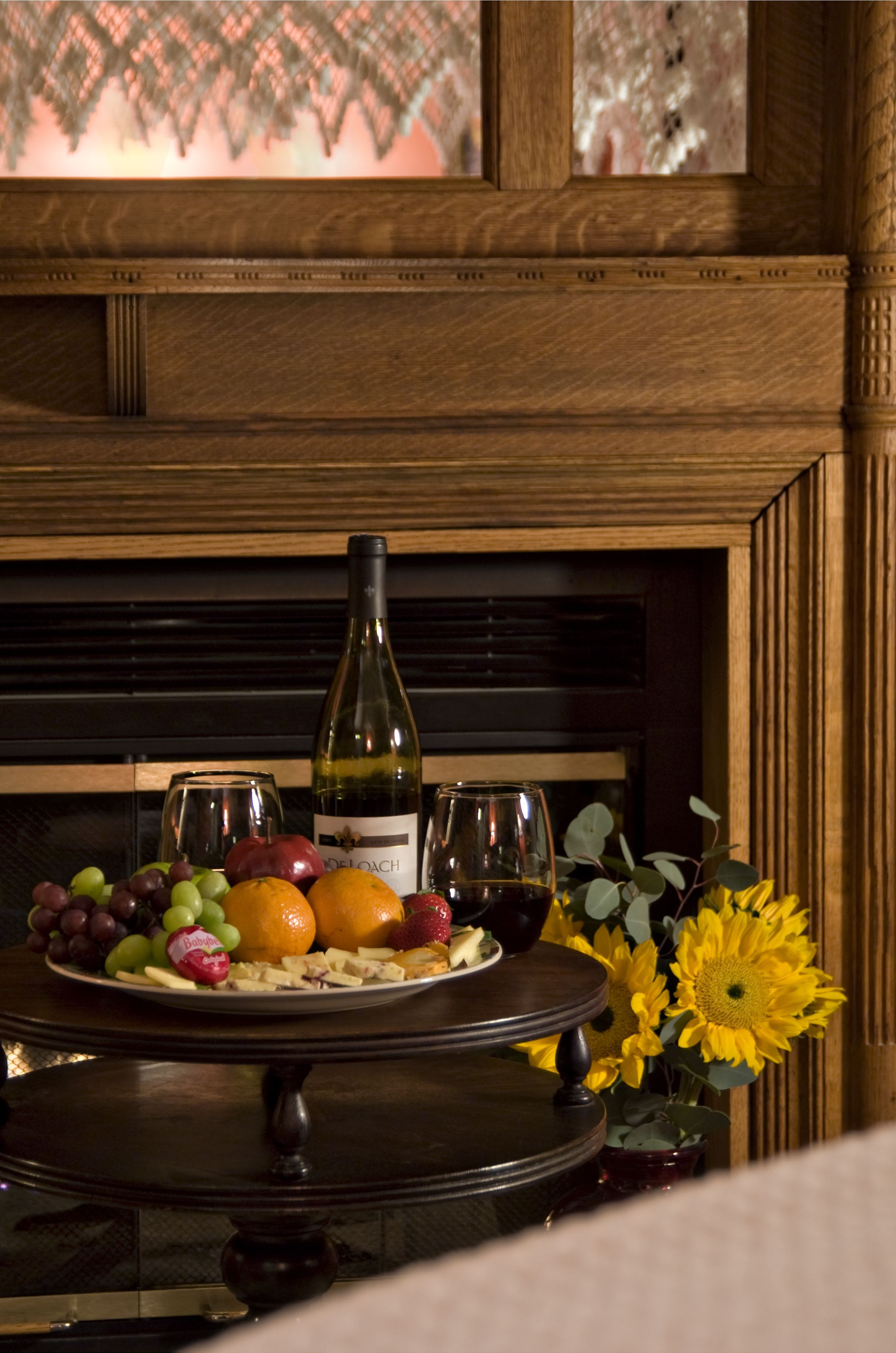 A wooden table with a wine bottle, glasses, and a fruit platter.