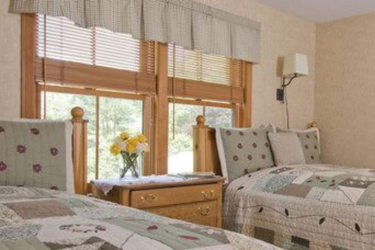 A bedroom with two beds, a nightstand, a dresser, and a window with blinds.