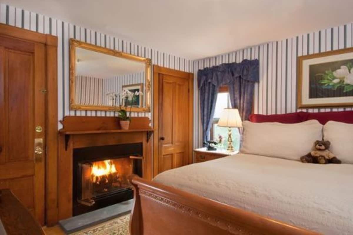 A hotel room with a fireplace, a large bed, a mirror, and a window with curtains.