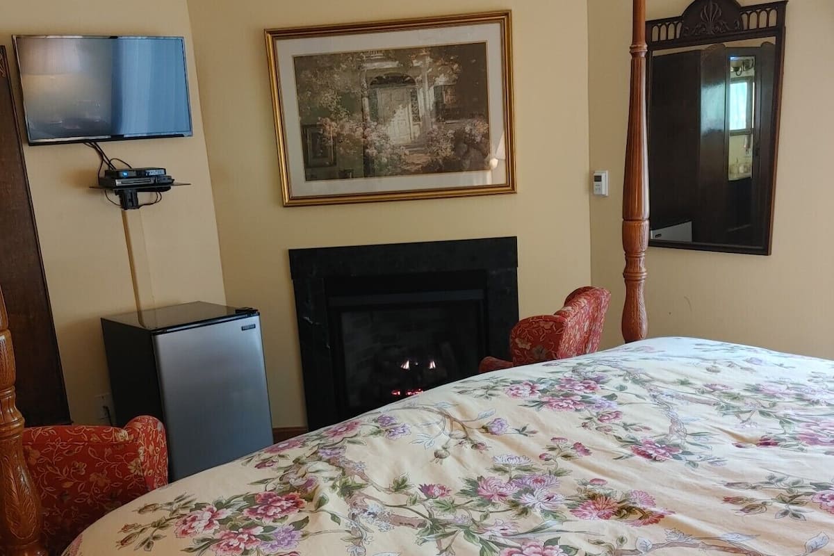 A hotel room with a large bed, a fireplace, a television, and a framed picture on the wall.