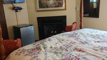 A hotel room with a large bed, a fireplace, a television, and a framed picture on the wall.
