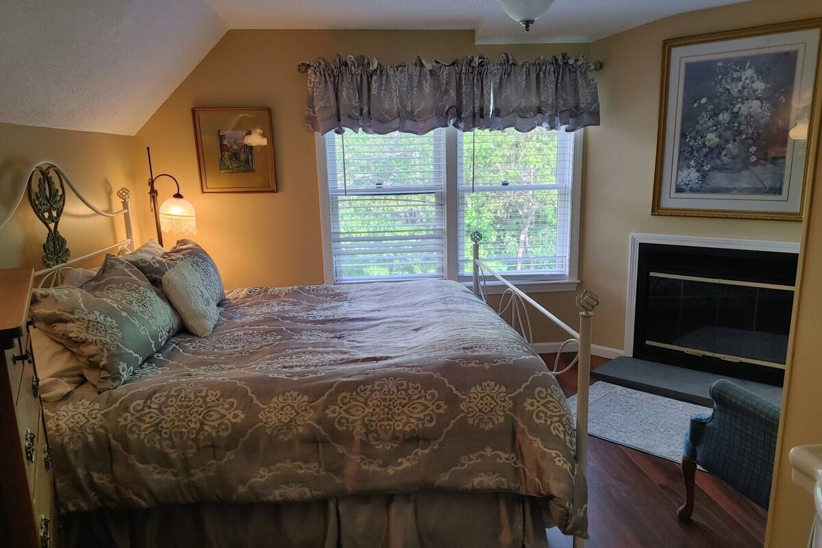 A bedroom with a bed, a window with blinds, a fireplace, and a framed picture on the wall.