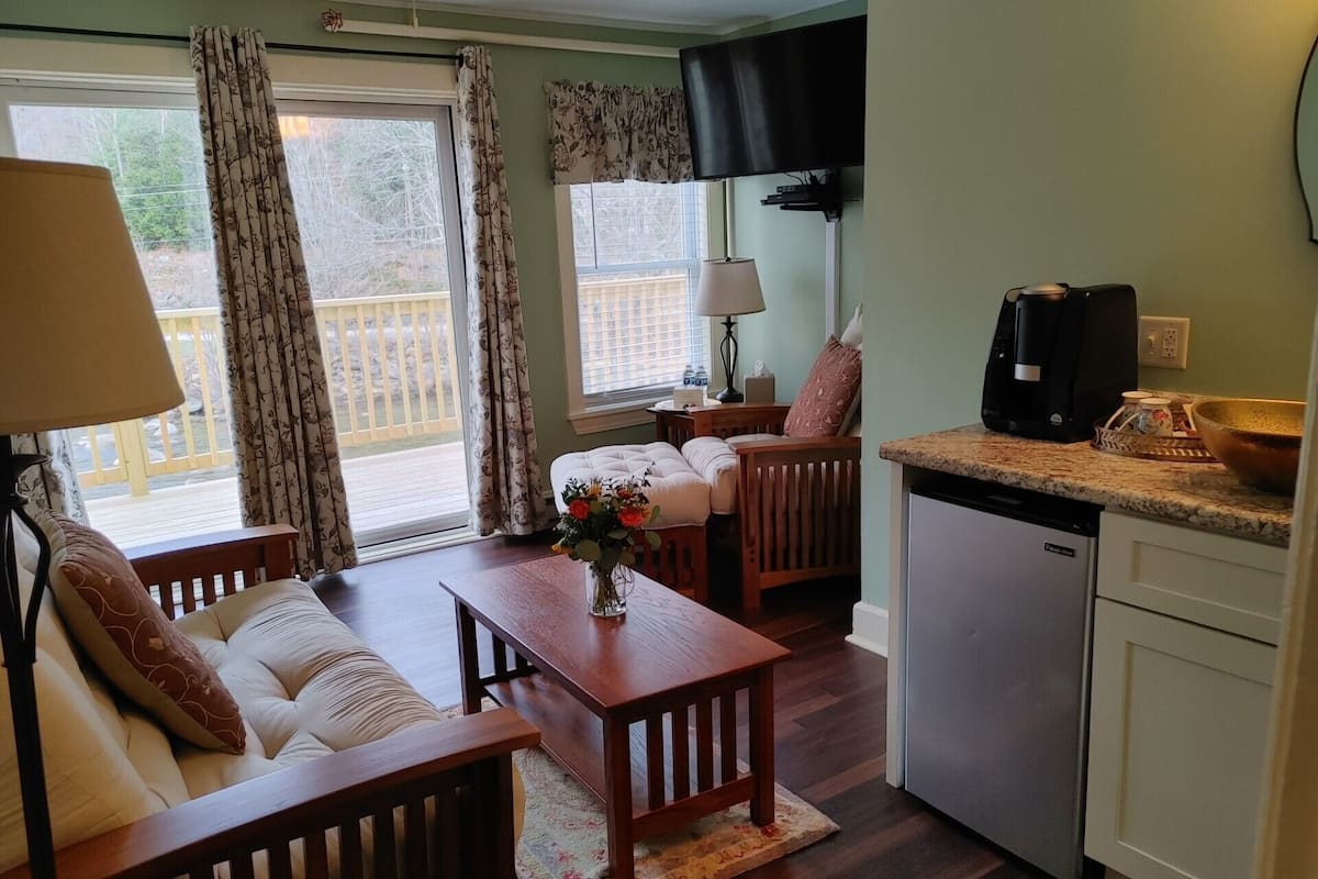 A cozy room with a wooden dining table, a sofa, a kitchen area with a dishwasher, and a TV mounted on the wall.