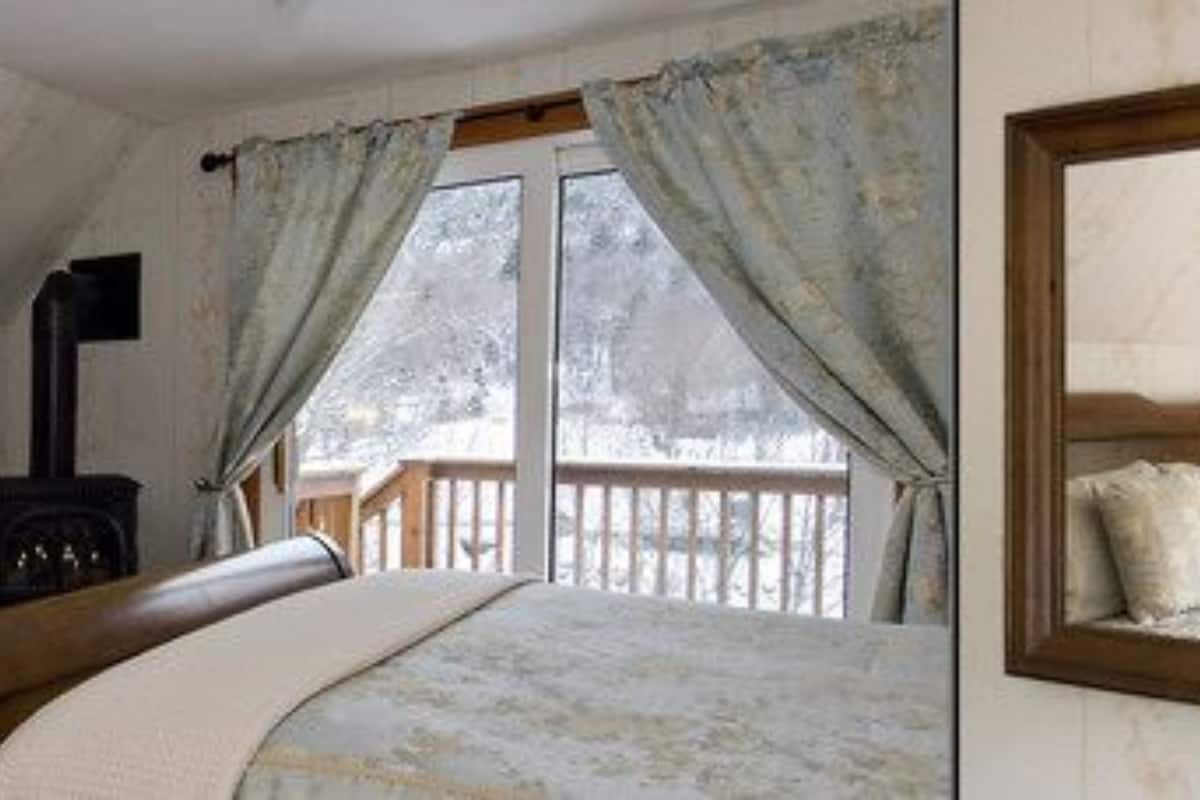 A bedroom with a large bed, a wooden headboard, a dresser, a mirror, and a window with curtains.
