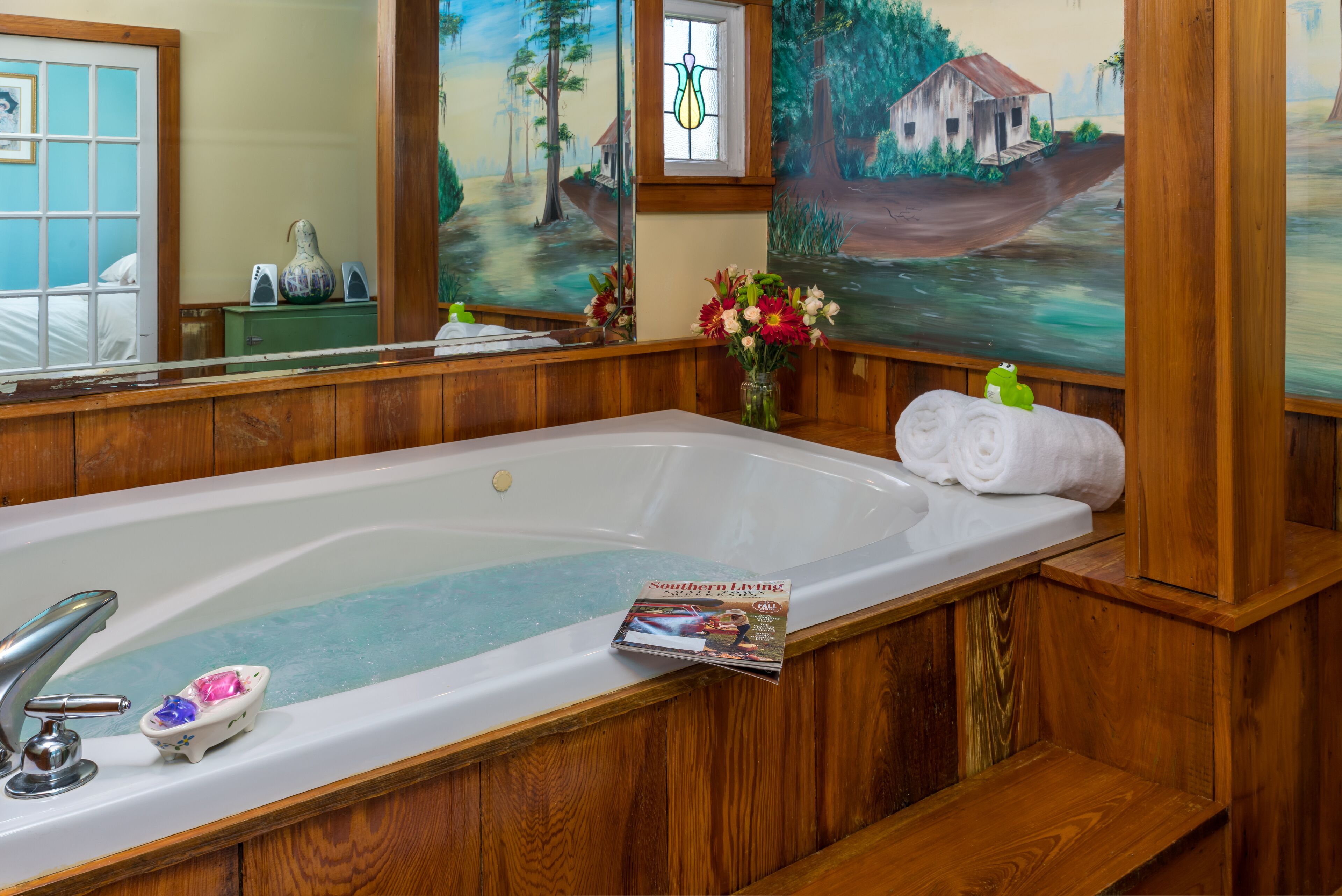 Un baño con una bañera grande, paneles de madera, un espejo y un cuadro de un paisaje rural.