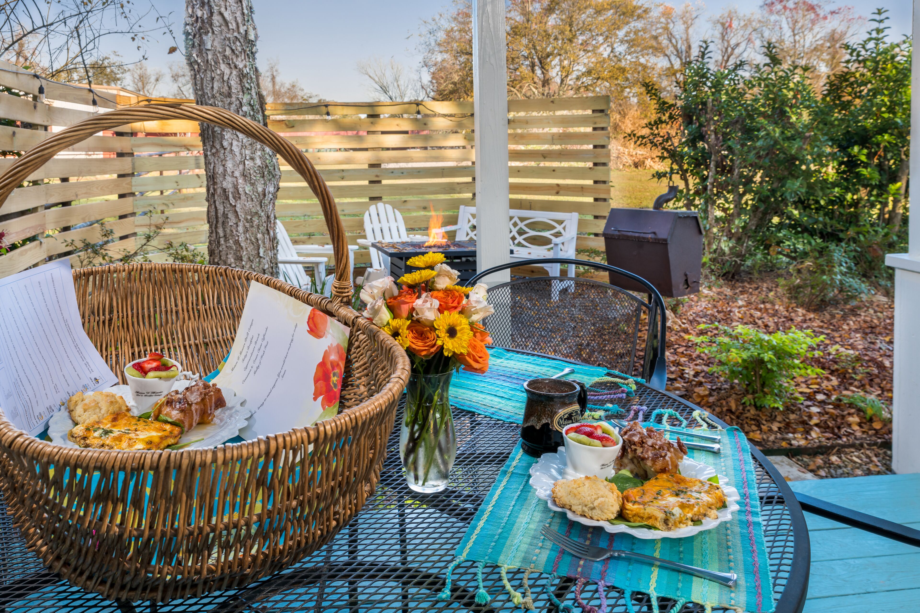 Un espace de restauration en plein air agrémenté d’un panier en osier, d’un vase de fleurs et d’une table dressée avec de la nourriture et des boissons.