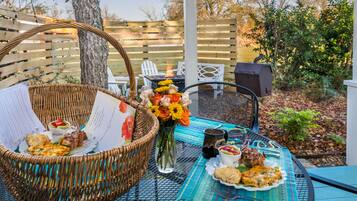 Un espace de restauration en plein air agrémenté d’un panier en osier, d’un vase de fleurs et d’une table dressée avec de la nourriture et des boissons.