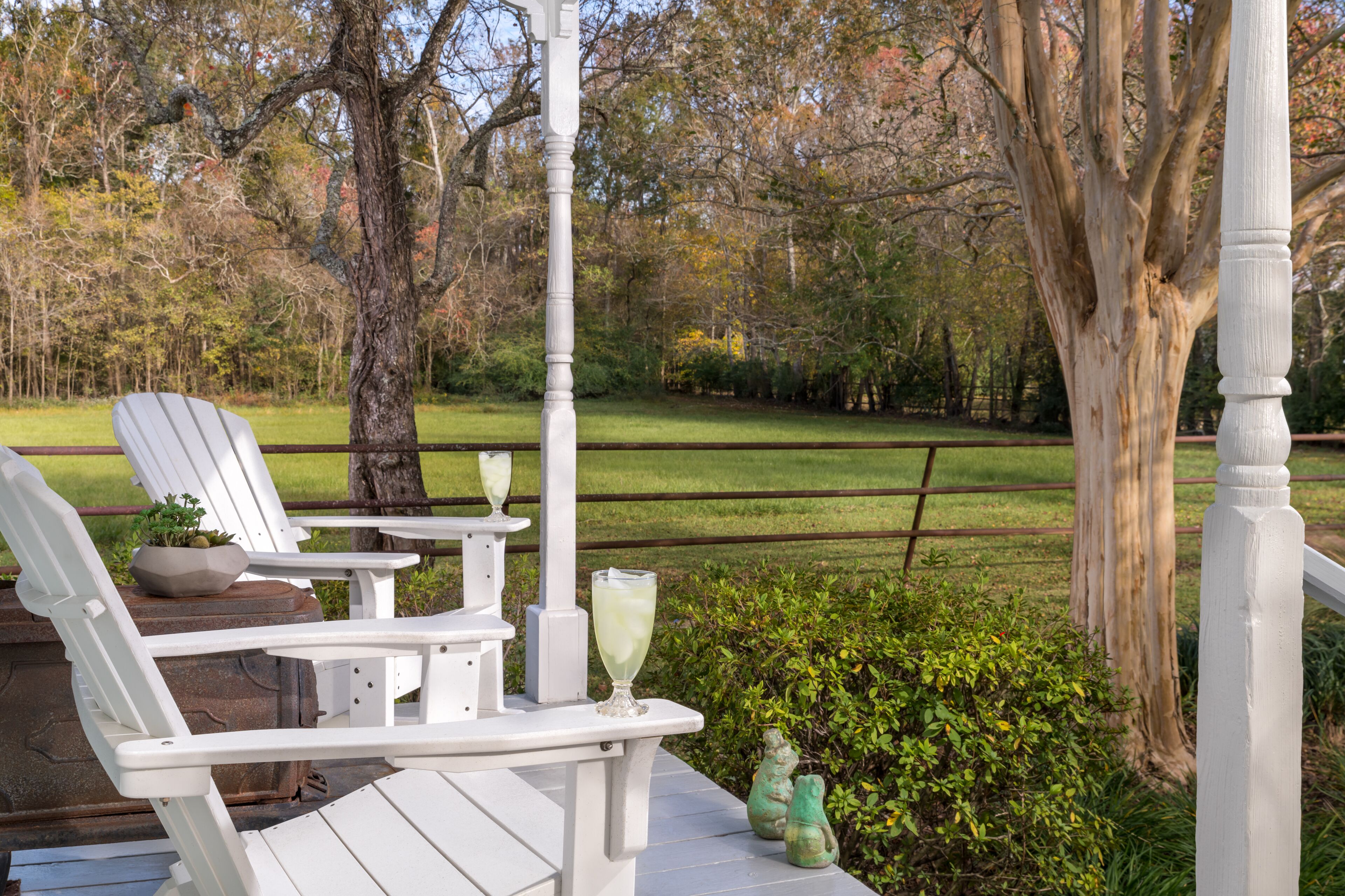 Un patio con mobiliario blanco, incluyendo sillas y una mesa, con árboles y una zona cubierta de césped de fondo.