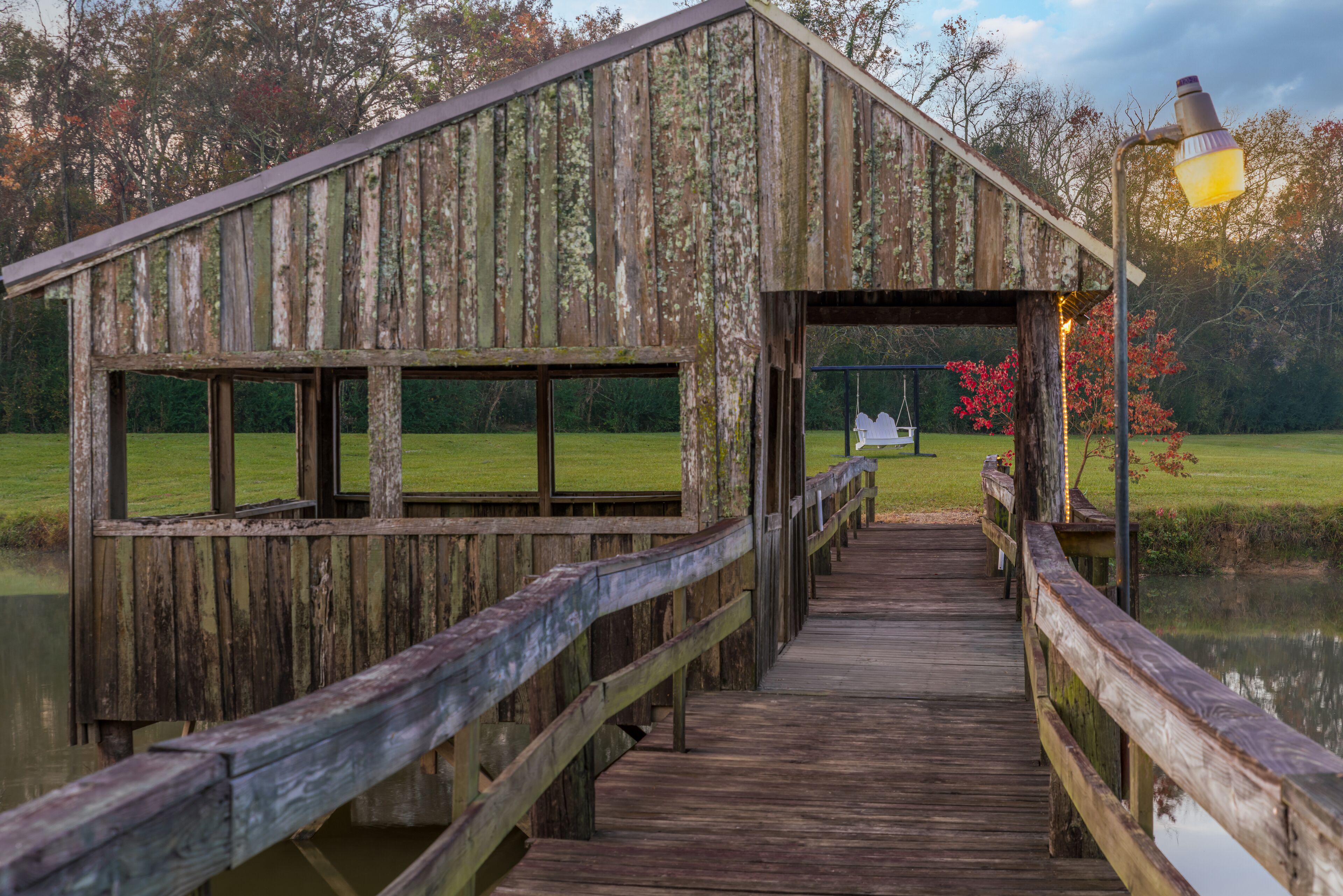 A wooden pier leading to a rustic wooden structure with a metal railing and a street lamp.