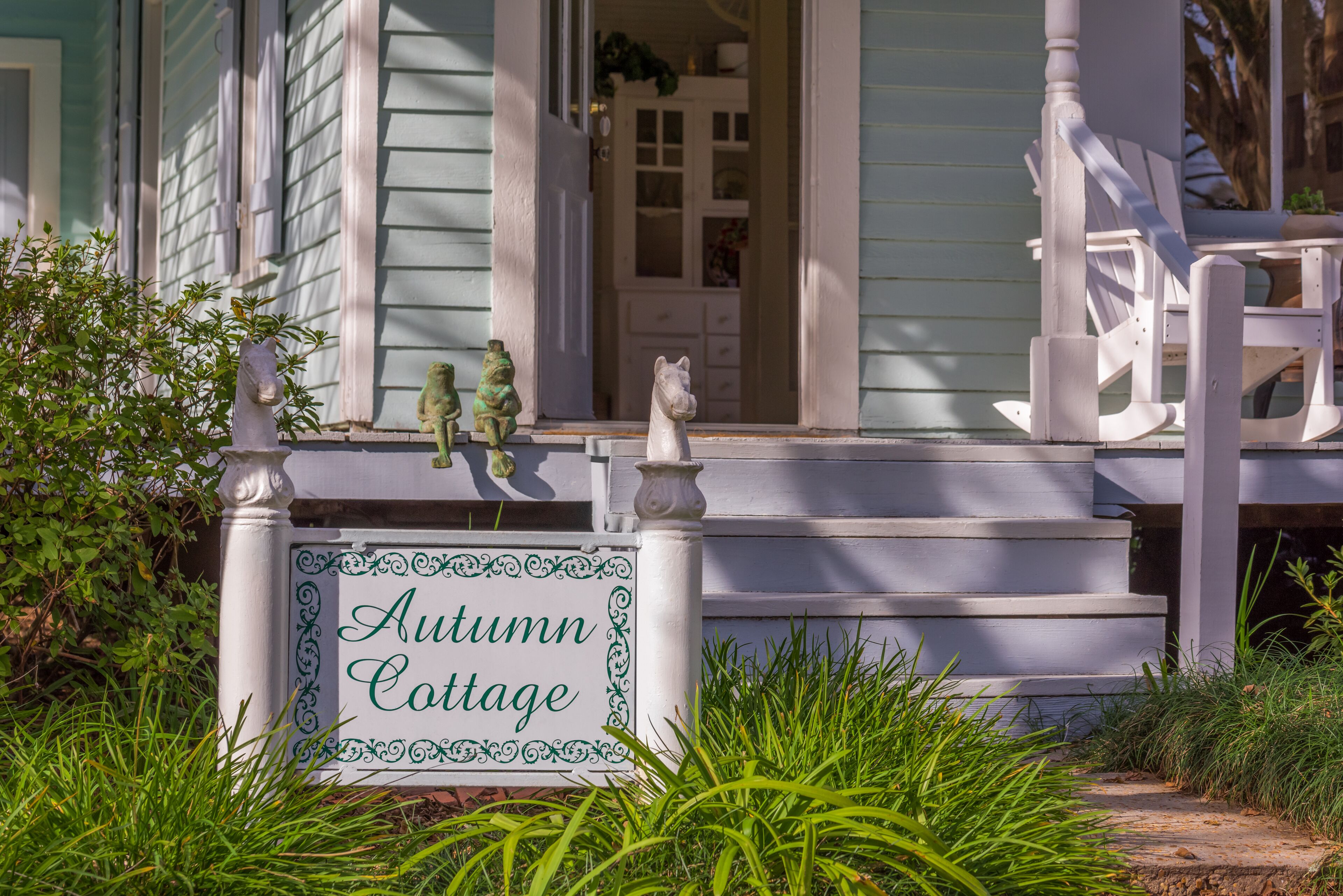 A porch with a sign reading "Autumn Cottage," a white chair, and a small statue.