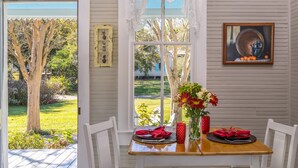 Uma sala de jantar com uma mesa posta para dois, um vaso com flores e um quadro na parede.