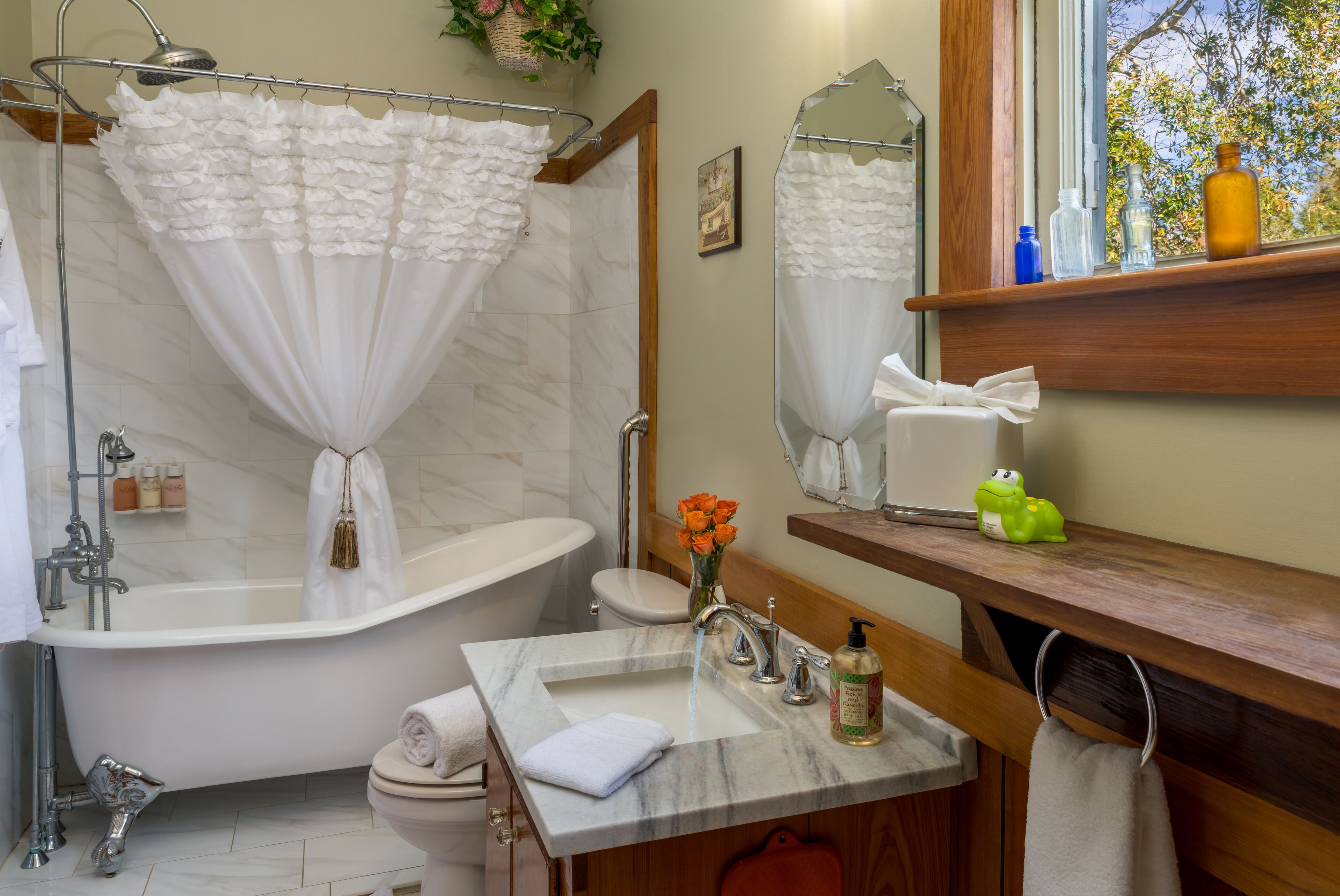 A bathroom with a freestanding bathtub, a sink with a marble countertop, a toilet, and a window with a view of trees.