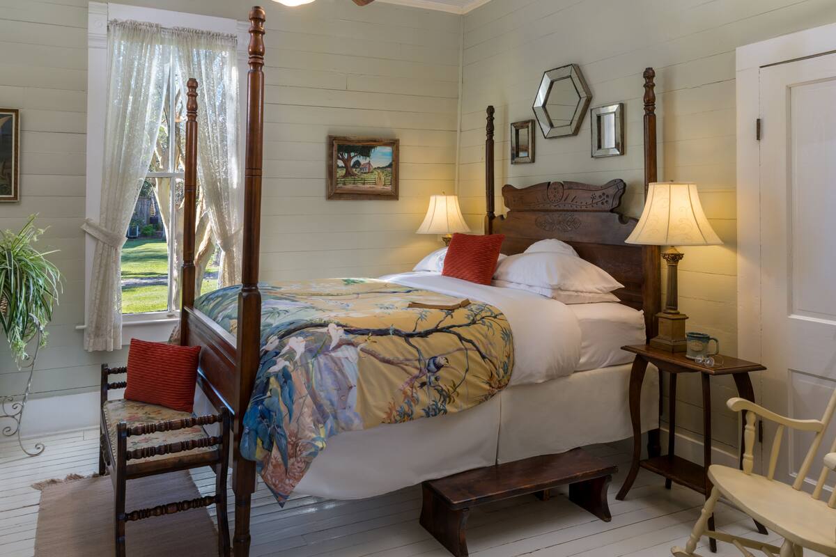 A traditional bedroom with a four-poster bed, two bedside tables with lamps, a wooden bench, and a chair.