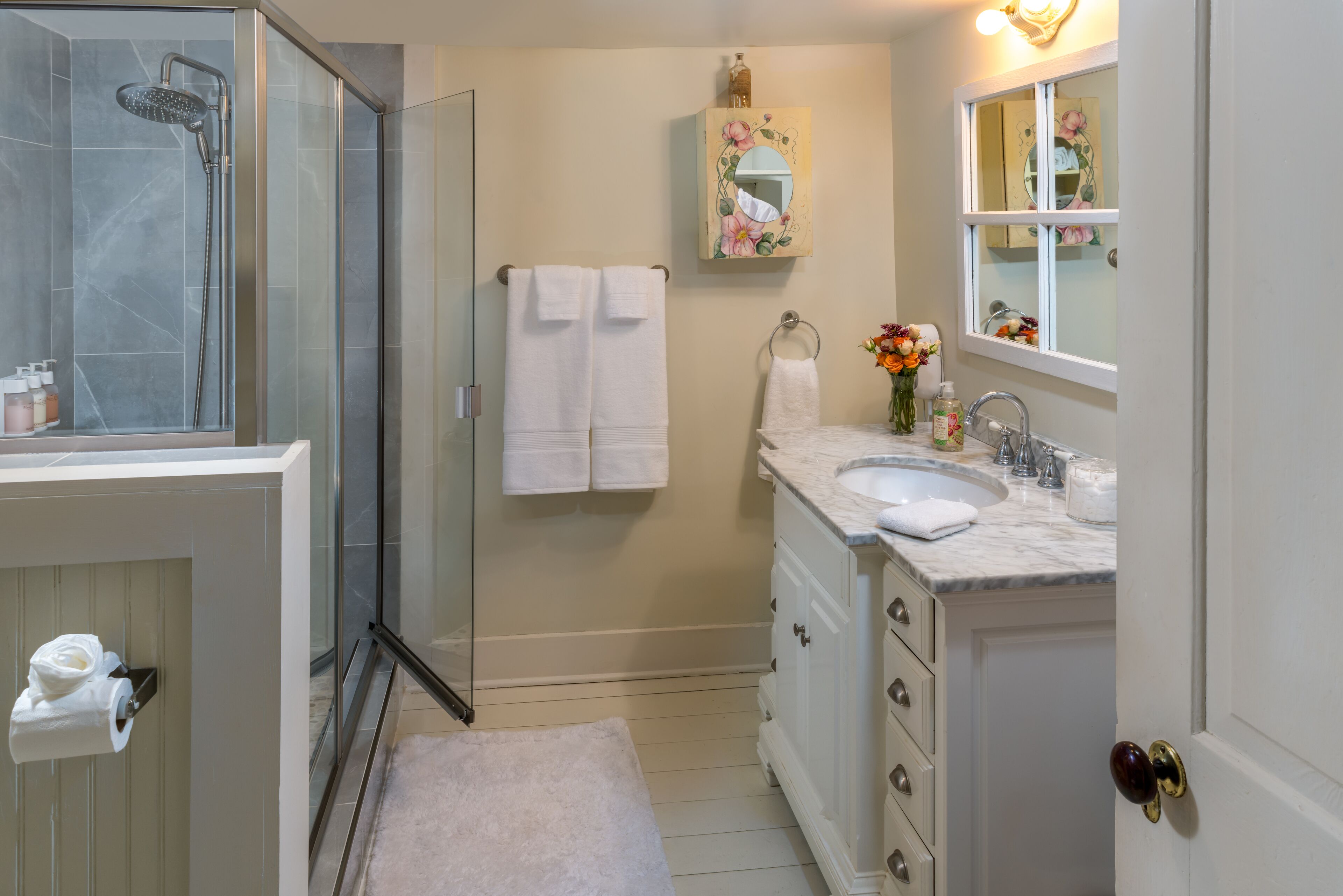 Un baño con cabina de ducha de vidrio, un lavabo con encimera de mármol y un mueble de tocador con cajones.