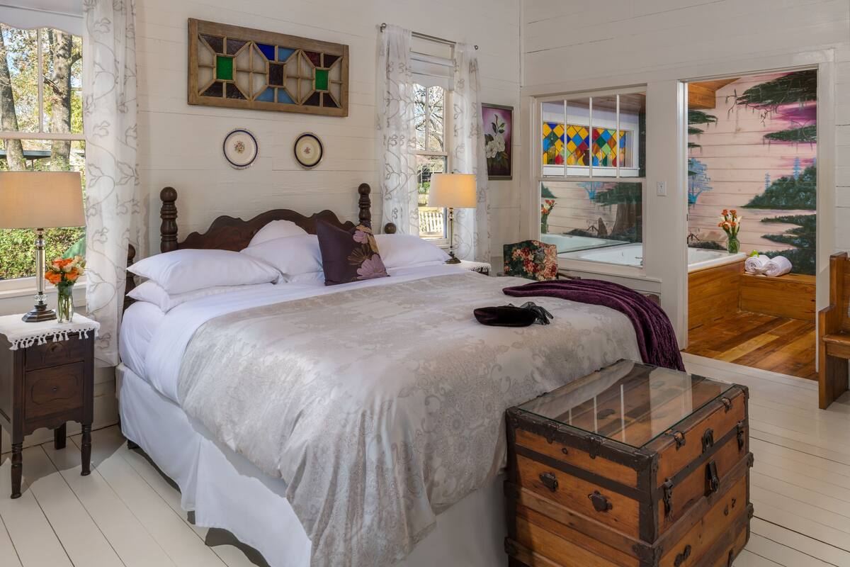 A bedroom with a large bed, a wooden dresser, and a window with a view of a wooden structure.