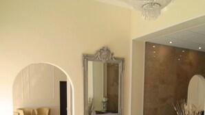 Un vestíbulo espacioso con piso de mármol, un espejo grande y ornamentado, y un candelabro. Hay sillones de cuero y un mostrador de recepción.