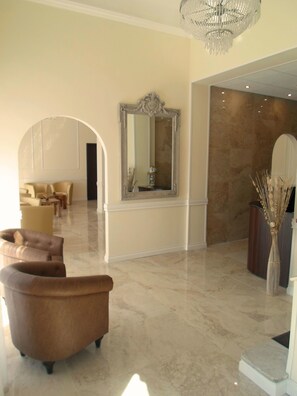 A spacious lobby with a marble floor, a large ornate mirror, and a chandelier. There are leather armchairs and a reception desk. - Hotel Regina Margherita (Bordighera)