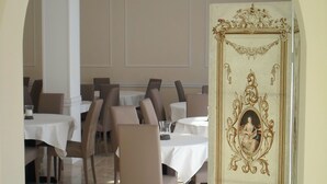 Un comedor con mesas y sillas, una araña y un espejo decorativo con un marco ornamentado.