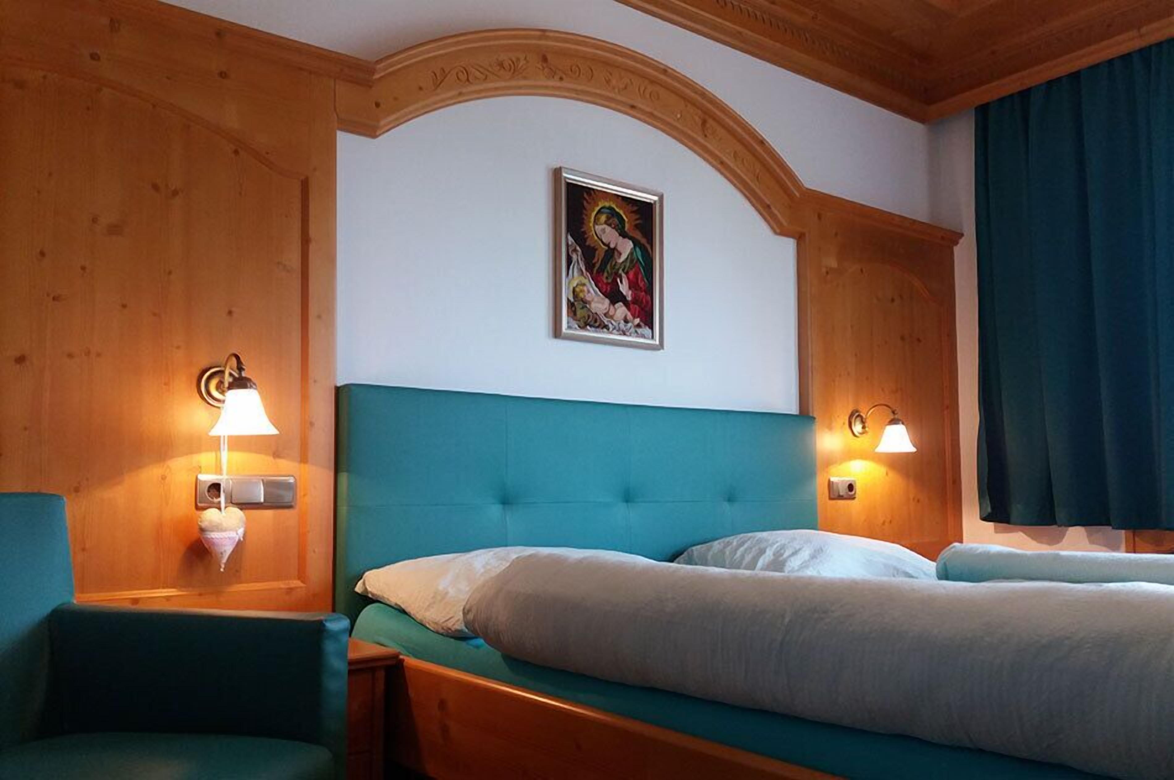Una camera d'albergo con soffitto in legno, una testiera imbottita color petrolio, due letti e lampade a parete.