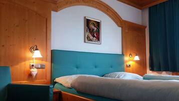 Una camera d'albergo con soffitto in legno, una testiera imbottita color petrolio, due letti e lampade a parete.