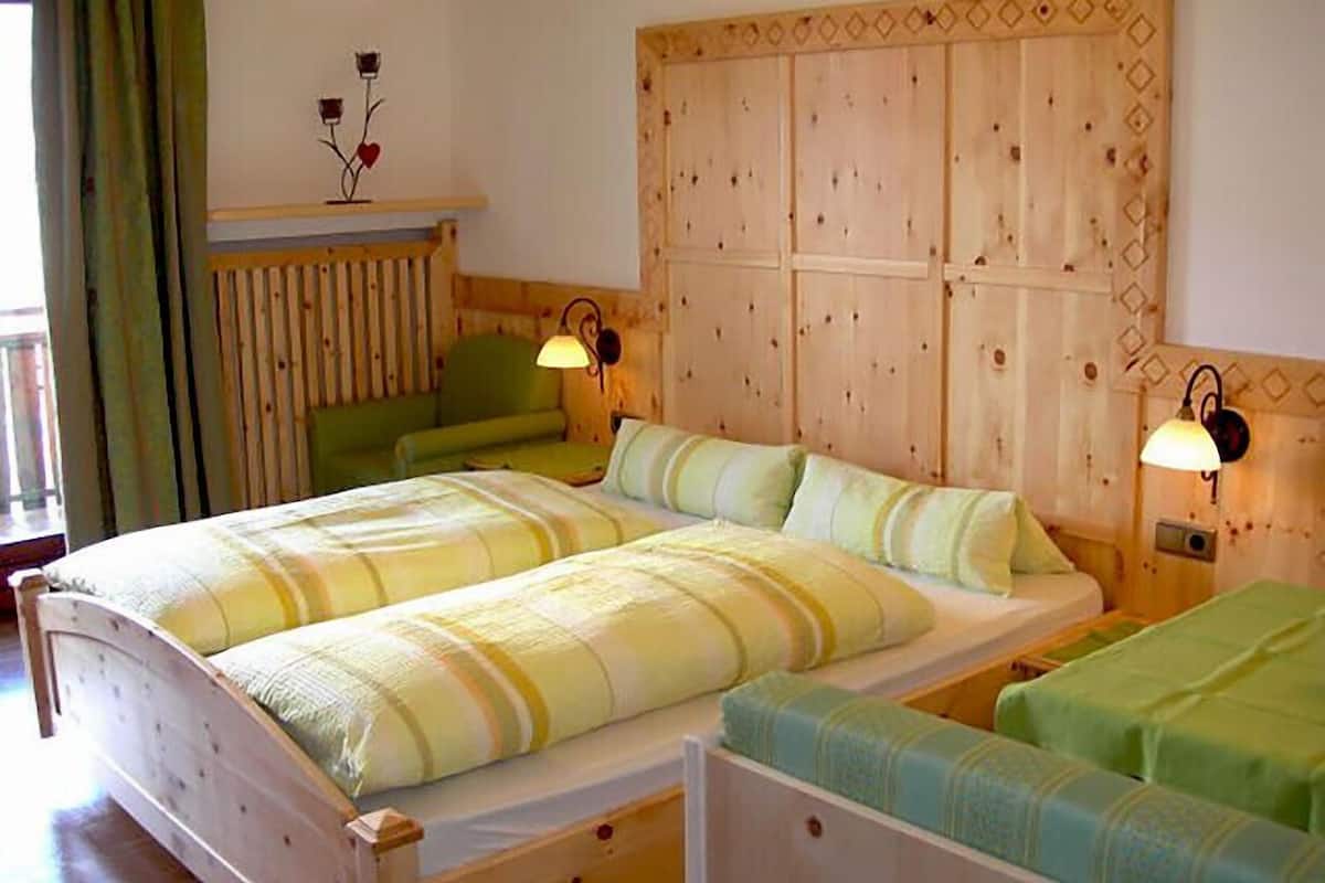 A room with a wooden headboard, two beds with striped bedding, a green chair, and two wall-mounted lamps.