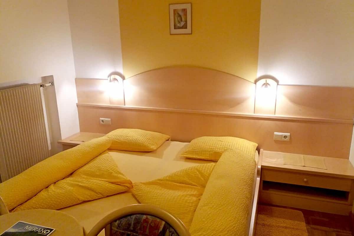 A hotel room with a bed, bedside tables, and a headboard with wall-mounted lights.