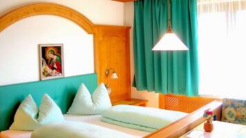 Une chambre d’hôtel avec un lit, une tête de lit en bois, un tableau, une fenêtre avec des rideaux et une table sur laquelle est posé un vase.