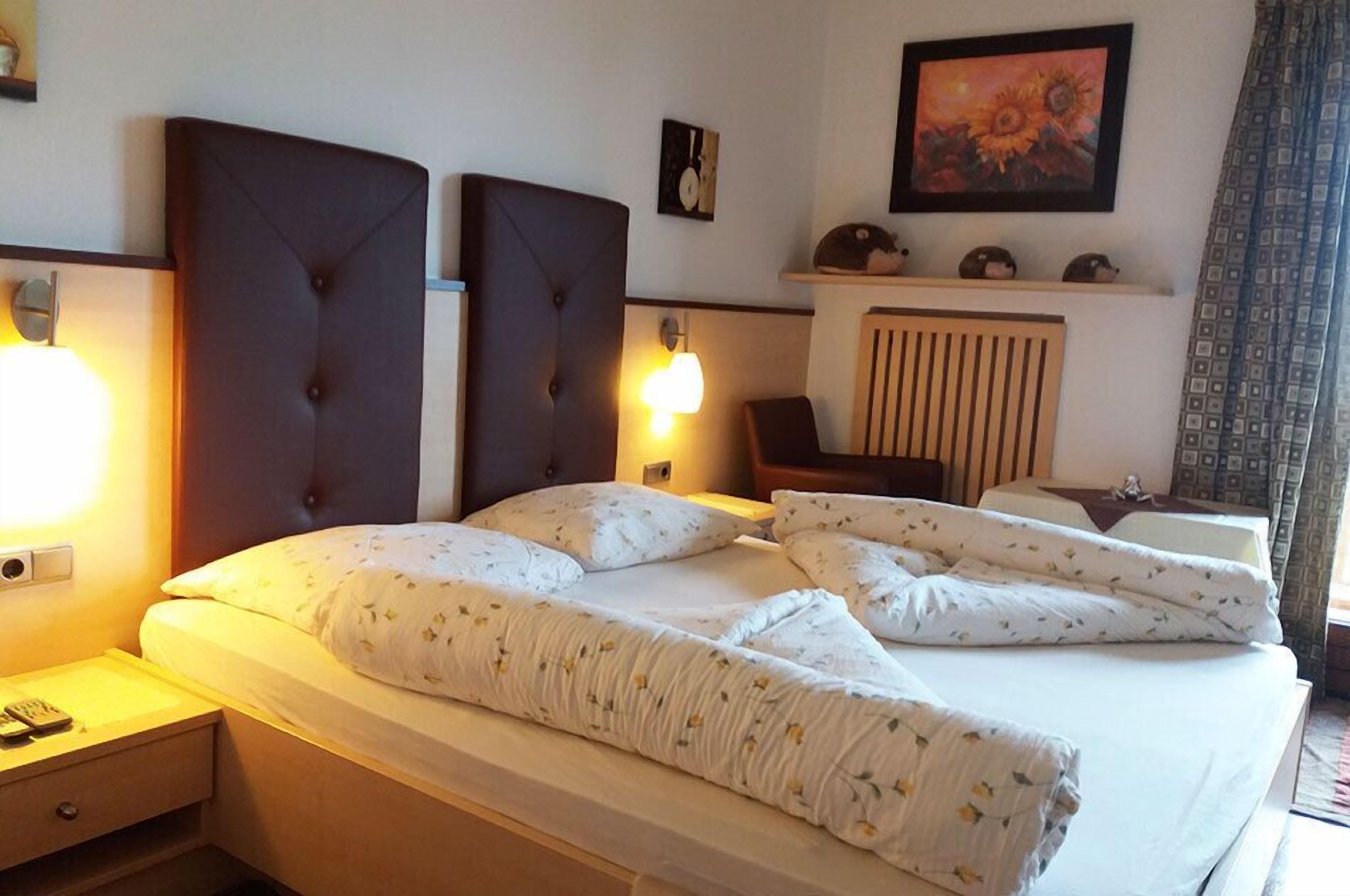 Una cama bien hecha con cabecera, lámparas de noche y un cuadro en la pared.