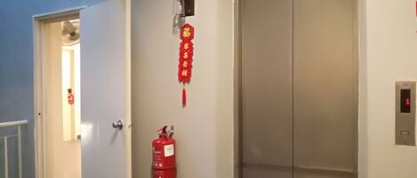 A hallway with an elevator, a fire extinguisher, and a door leading to another room.