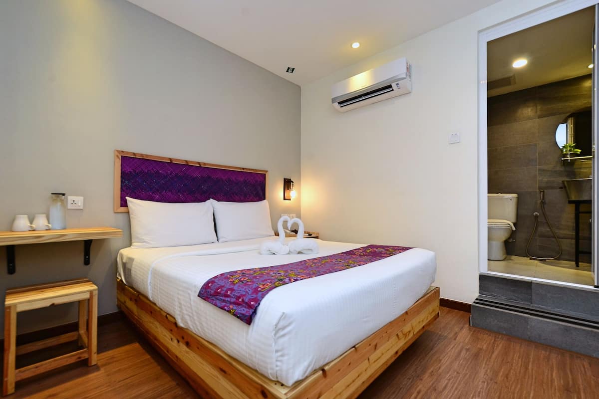 A modern bedroom with a wooden bed, white bedding, a purple decorative pillow, a small bedside table, and a nightstand.