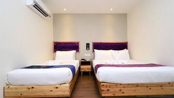 A hotel room with two wooden beds, white bedding, purple headboards, and an air conditioning unit on the wall.