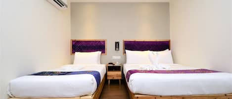 A hotel room with two wooden beds, white bedding, purple headboards, and an air conditioning unit on the wall.