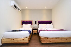 A hotel room with two wooden beds, white bedding, purple headboards, and an air conditioning unit on the wall.