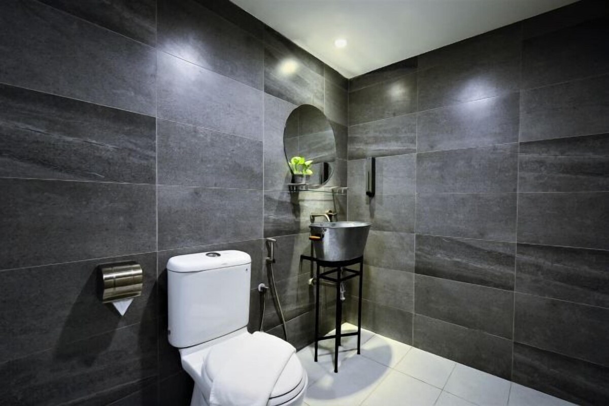 A modern bathroom with dark tiles, a white toilet, a sink on a pedestal, and a shower area.