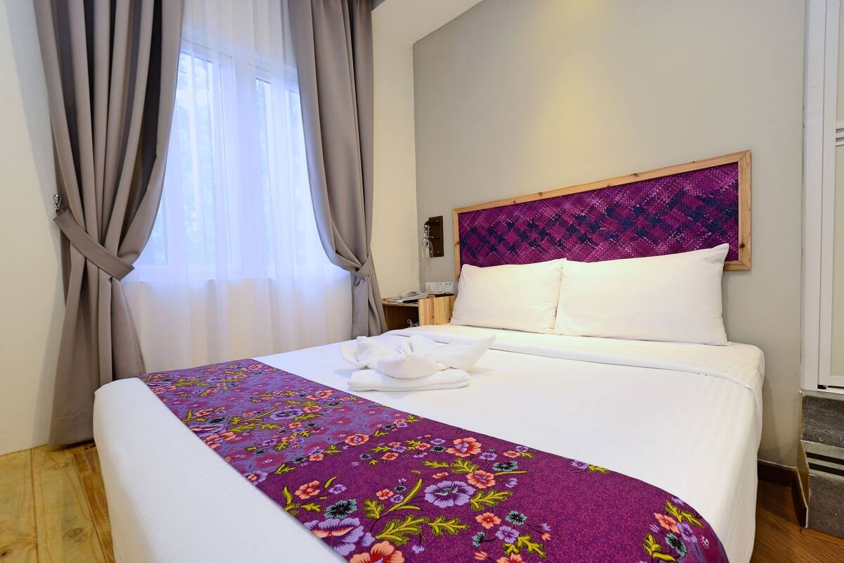 A neatly made bed with a floral bedspread, a headboard with a woven pattern, and a window with curtains.