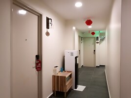 Egy folyosó, amelyen egy fa pad, egy hűtőszekrény és egy tűzjelzővel ellátott ajtó található.