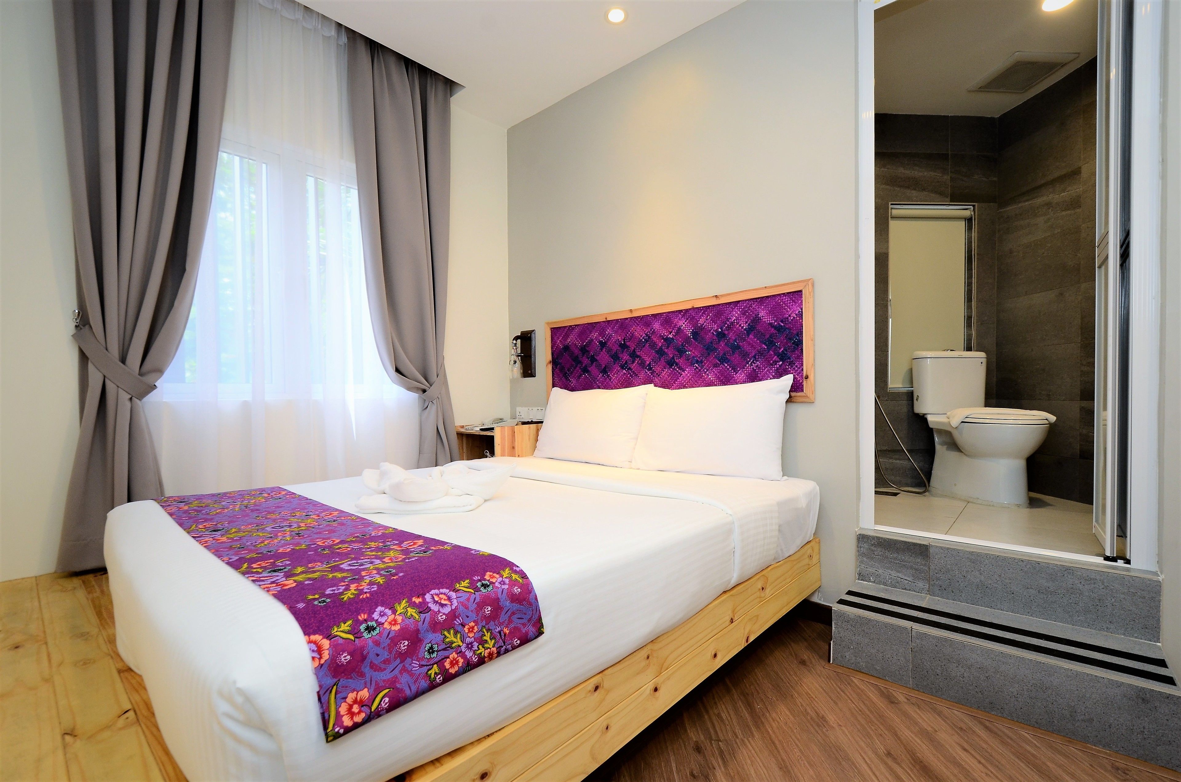 A neatly made bed with a floral bedspread, a wooden headboard, and a bathroom visible through an open door.