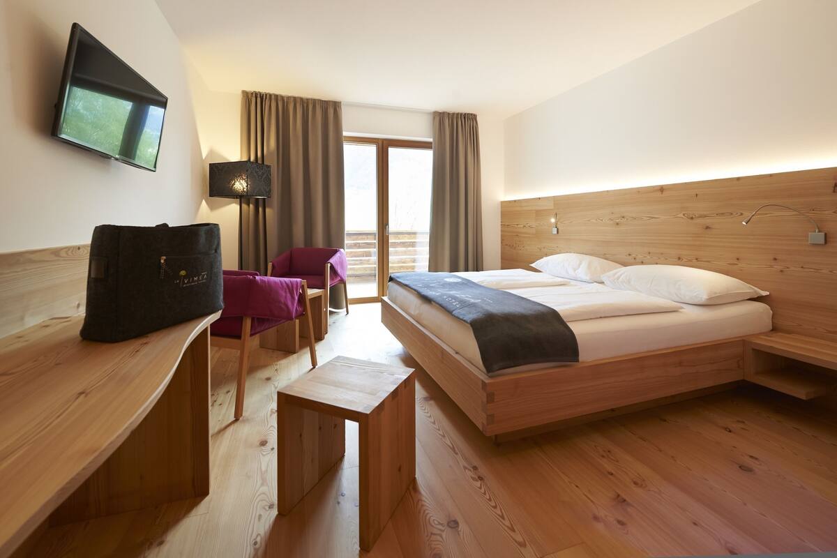 A hotel room with a bed, a desk, a chair, a TV, and a balcony with curtains.