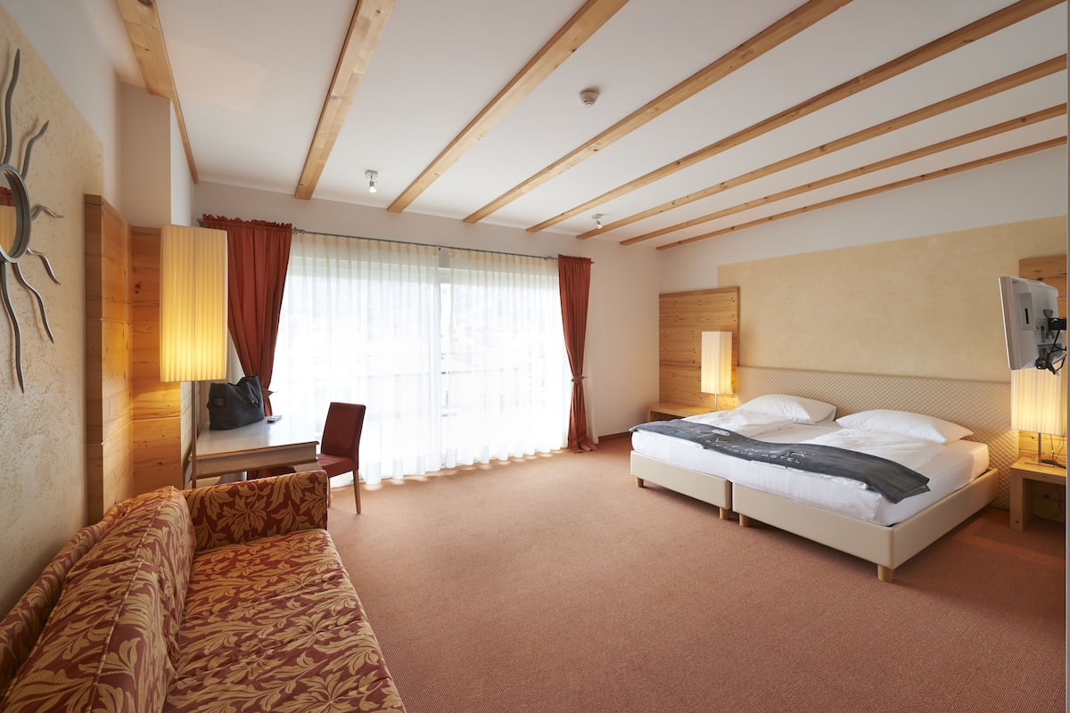 A hotel room with a bed, a sofa, a desk, and a chair.