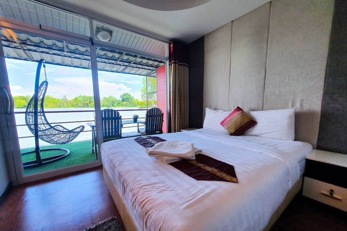 Een slaapkamer met een groot bed, uitzicht op de omgeving en een balkon met stoelen.
