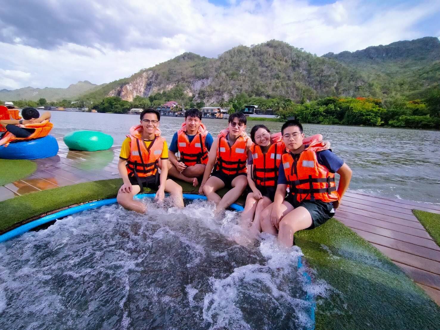 A group of people sitting on a floating platform with a water slide, surrounded by a lake and hills.