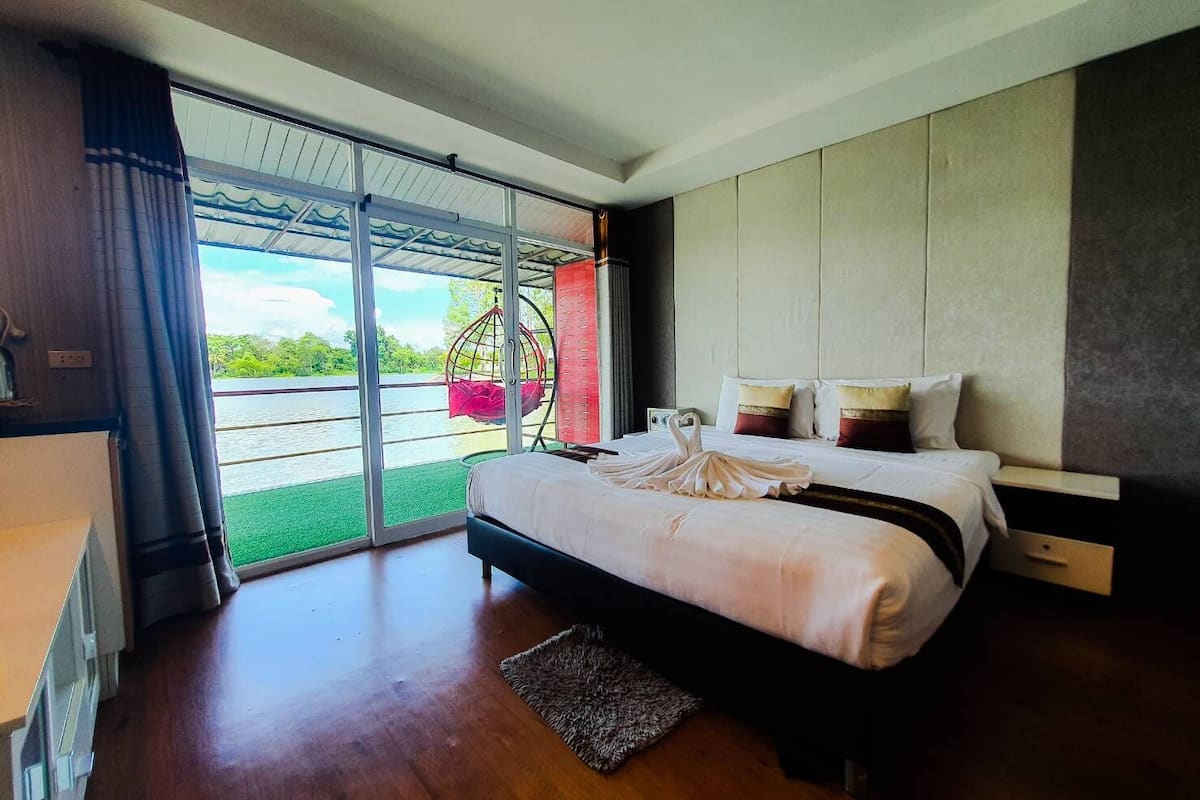 Een moderne slaapkamer met een groot bed, een schommelstoel bij het raam en uitzicht op een waterpartij.