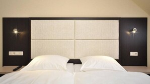 A hotel room with a large bed, a headboard with a light panel, and a remote control on the nightstand. - Bova Hotel Frankfurt (Frankfurt)