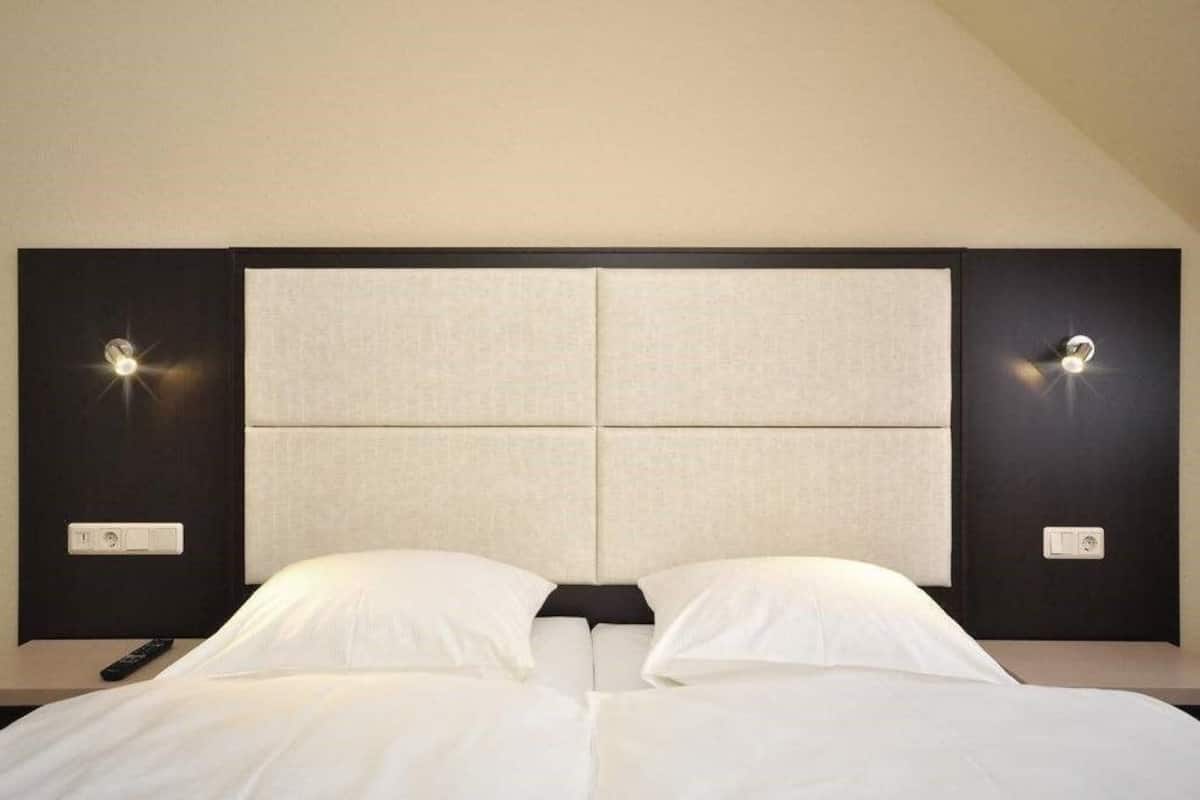 Quarto de hotel com uma cama grande, cabeceira com painel de luz e controle remoto no criado-mudo.
